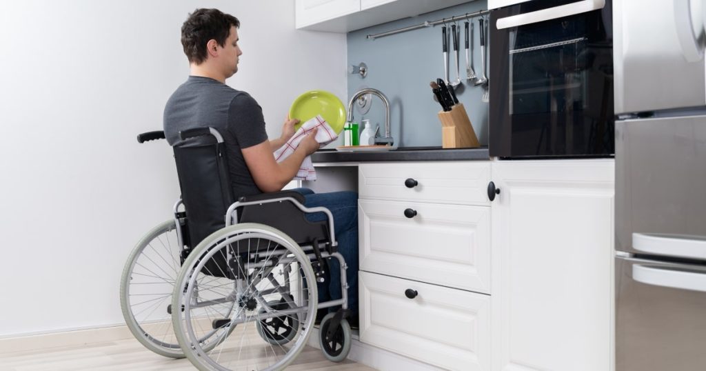 A man in a wheelchair doing the dishes in a disabled access kitchen design.
