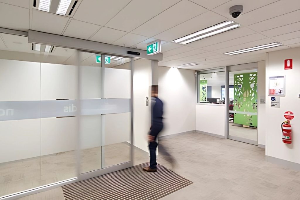 STA21 automatic sliding doors gallery 4 Man walking through a motion-activated sliding door in a commercial workplace.