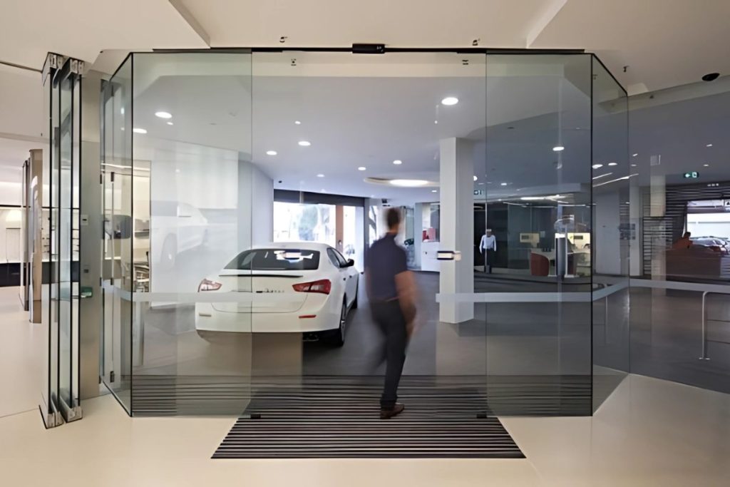 Person walking through full-glass automatic sliding doors in a luxury car showroom.